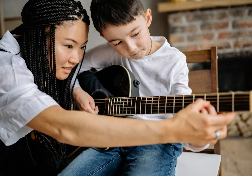 Cô giáo cầm tay hướng dẫn bé chơi guitar